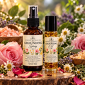 Two bottles of 'Essence of Healing' Grounding Oil and Grounding Spray displayed on a rustic wood slice surrounded by pink roses, daisies, and other wildflowers in a garden setting.