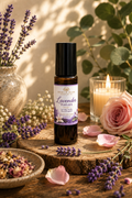 Lavender Fields Aromatherapy essential oil bottle displayed on a rustic wood slice surrounded by lavender sprigs, pink rose petals, a lit candle, dried flowers, and green foliage.