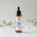Bottle of 'Essence of Healing' with a dropper on a light background with greenery. Lilac Nights scented body drops 