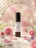 A dark amber roll-on bottle labeled 'Essence of Healing Love Potion' stands centered on a marble surface surrounded by pink roses, lavender sprigs, and scattered petals, with a soft pink bokeh background.